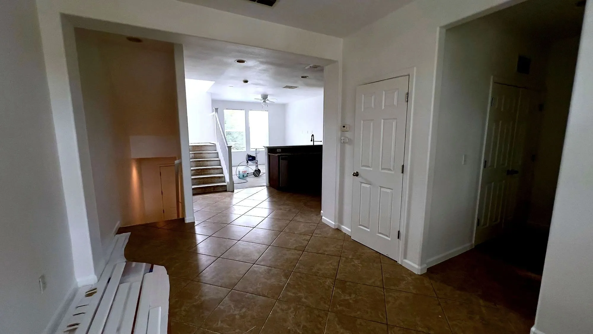 Freshly painted empty interior with new tile flooring, looking through to a kitchen and staircase