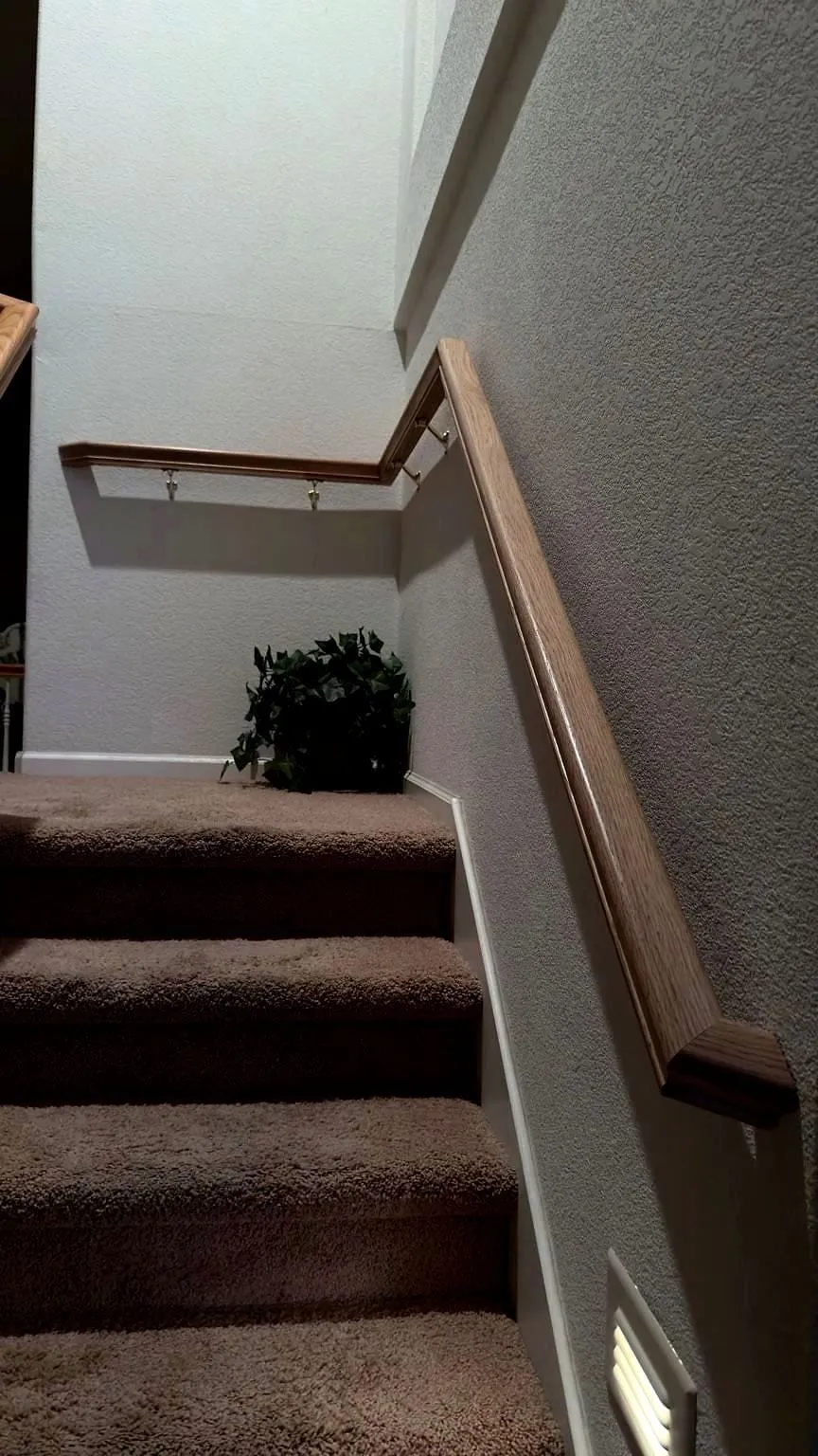 Oak handrail on brass brackets and fresh white baseboard along a carpeted staircase wall